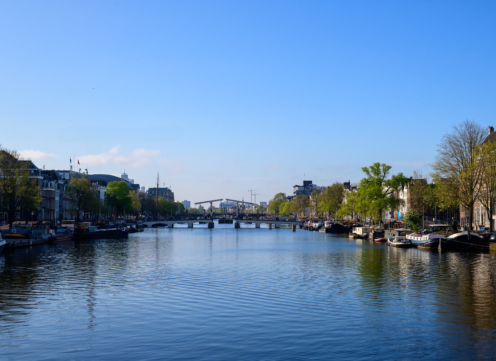 Blue Expanse Daytime view down the Amstel River toward the Magere Brug with moored boats along both banks.
