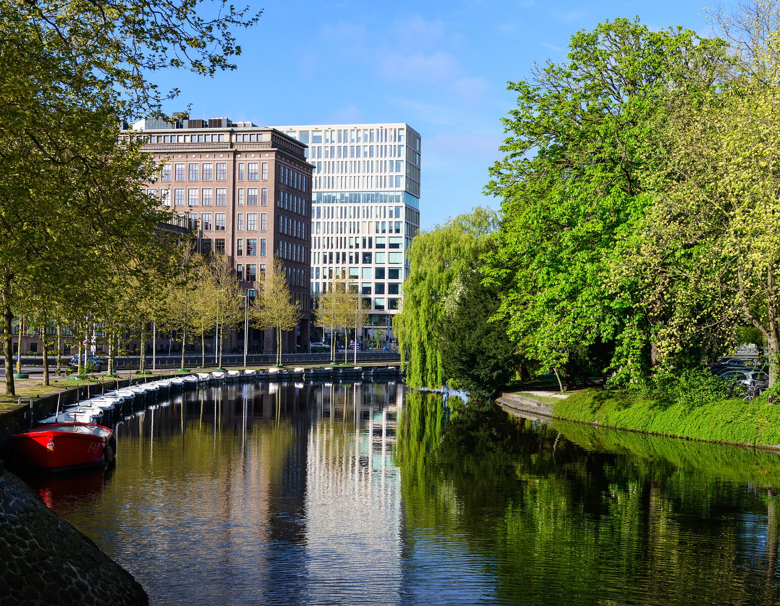 Riverside Curve Calm Amsterdam canal bend framed by leafy trees and mixed historic-modern buildings mirrored in the water.