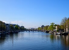 Blue Expanse Daytime view down the Amstel River toward the Magere Brug with moored boats along both banks.