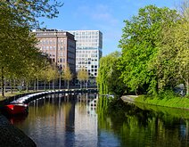 Riverside Curve Calm Amsterdam canal bend framed by leafy trees and mixed historic-modern buildings mirrored in the water.