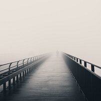 Endless Bridge Single person walks down a narrow railing footbridge that dissolves into blanketing fog.