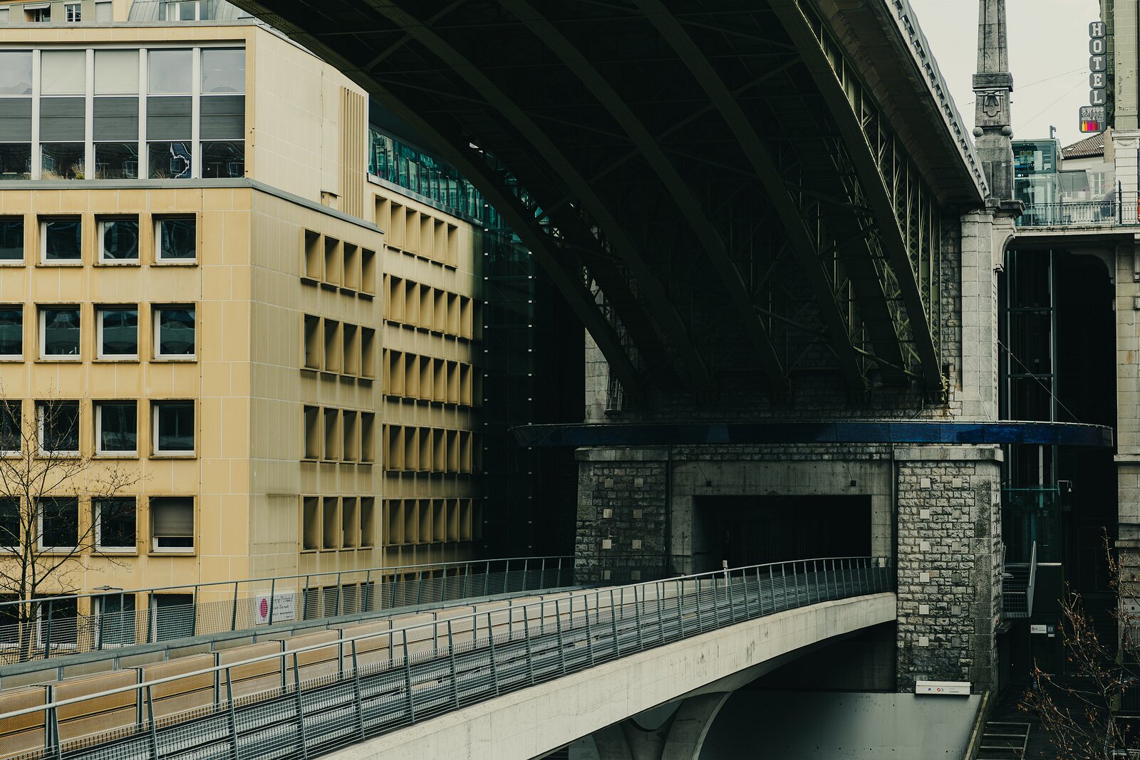 Urban Layers Yellow office block meets the underside of an elevated bridge in a layered city scene.