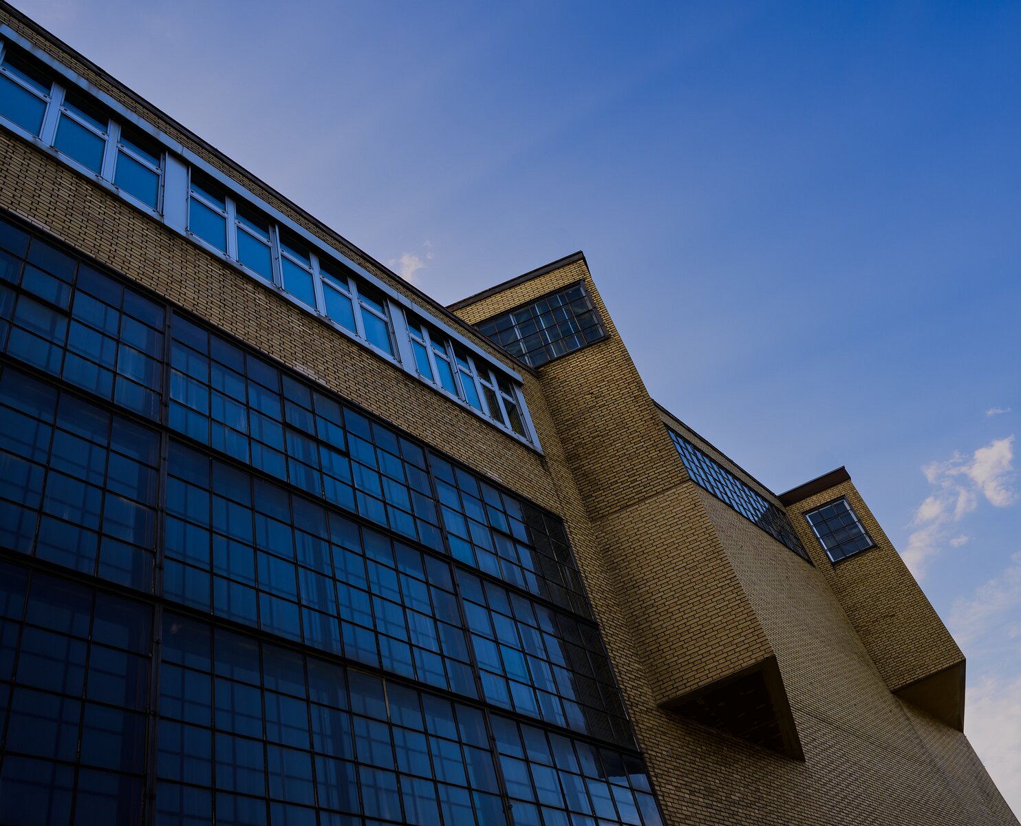 Bold Perspective Sunlit yellow-brick industrial building with expansive blue-tinted windows under a clear blue sky.