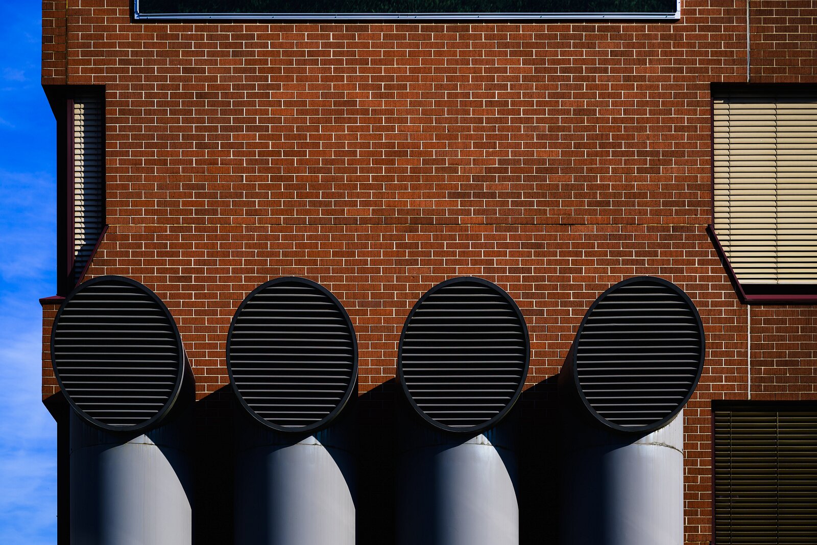 Symmetric Vents Four large circular ventilation ducts protrude in a row from a red brick wall in stark sunlight.