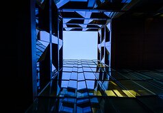 Geometric Void Looking upward through an angular glass atrium toward a square opening of clear sky.