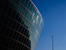 Modern Curve Rounded glass office building arcs into a bright blue sky beside a solitary lamppost.