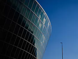 Modern Curve Rounded glass office building arcs into a bright blue sky beside a solitary lamppost.