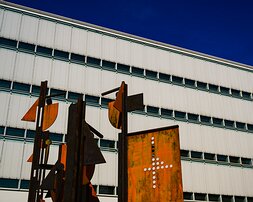 Industrial Artistry Weathered rust-colored abstract metal sculpture stands before a white modern office facade and deep blue sky.