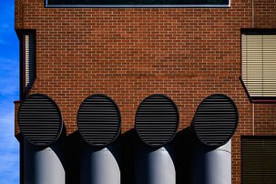 Symmetric Vents Four large circular ventilation ducts protrude in a row from a red brick wall in stark sunlight.