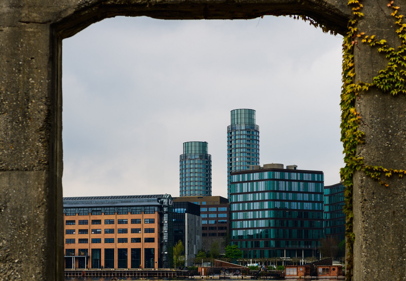 Concrete Window Twin cylindrical glass towers framed by weathered concrete arch on Copenhagen waterfront.