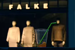Plastic Reverie A discarded plastic cup with a green straw sits in the foreground, while three softly lit mannequins stand blurred in a fashion store window behind it.