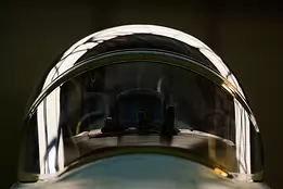 Cockpit Dome Front-facing close-up of a fighter jet canopy with hangar lights reflecting on the curved glass.