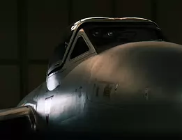 Hangar Sentinel Dimly lit side view of a vintage fighter jet’s nose and cockpit inside a hangar.