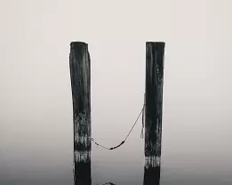 Tethered Quiet Two weathered wooden posts stand in calm water with a rope loosely connecting them, reflected in the still surface.