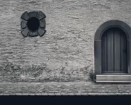 Arched Entry Rough stone wall with arched wooden door and small circular window.
