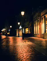 After the Rain Night photograph of a wet cobblestone street glowing with warm reflections from street lamps and storefront windows, creating a quiet and atmospheric scene.