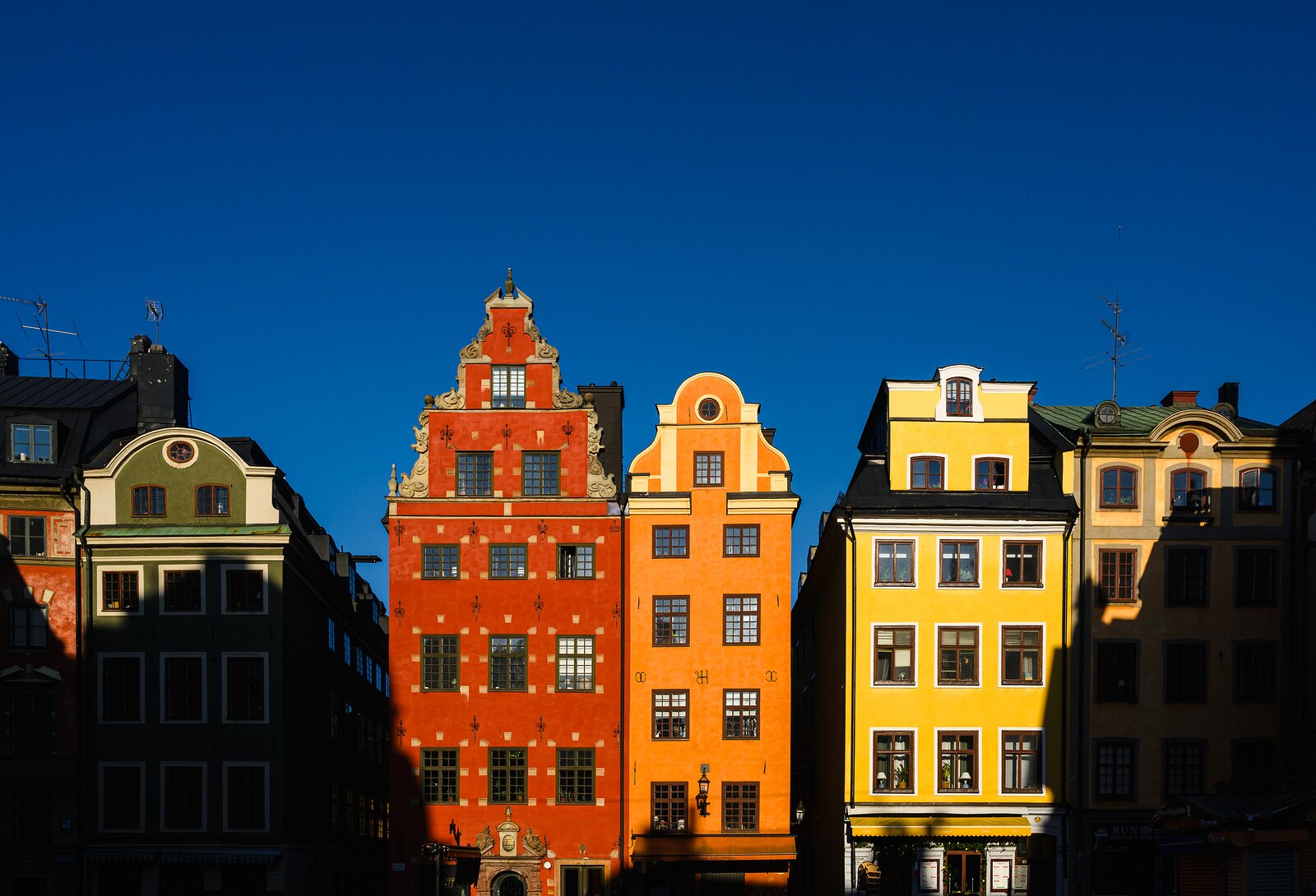 Color Row Iconic colored gabled houses line Stortorget square in Gamla Stan, sharply lit against a deep-blue morning sky.