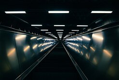 Tunnelbana Rise A long, lit escalator tunnel in Stockholm’s metro converges to a vanishing point deep underground.