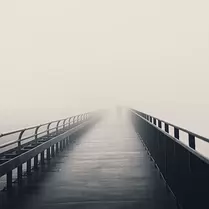 Endless Bridge Single person walks down a narrow railing footbridge that dissolves into blanketing fog.