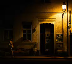 Silent Street Man walks past a dimly lit building under a glowing streetlamp at night.