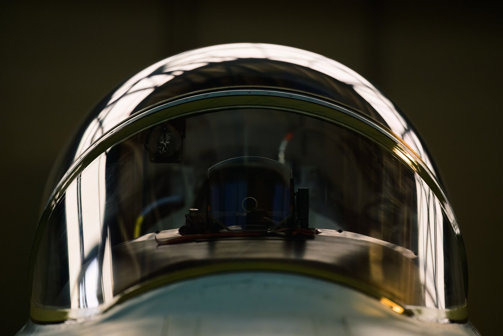 Cockpit Dome Front-facing close-up of a fighter jet canopy with hangar lights reflecting on the curved glass.
