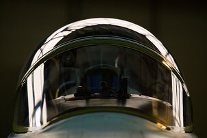 Cockpit Dome Front-facing close-up of a fighter jet canopy with hangar lights reflecting on the curved glass.