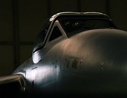 Hangar Sentinel Dimly lit side view of a vintage fighter jet’s nose and cockpit inside a hangar.