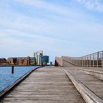 Curved Footbridge Wooden boardwalk sweeps over the harbor toward modern apartments in Copenhagen.