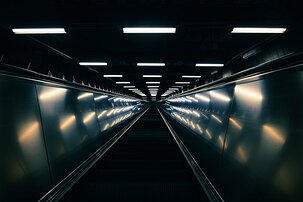 Tunnelbana Rise A long, lit escalator tunnel in Stockholm’s metro converges to a vanishing point deep underground.