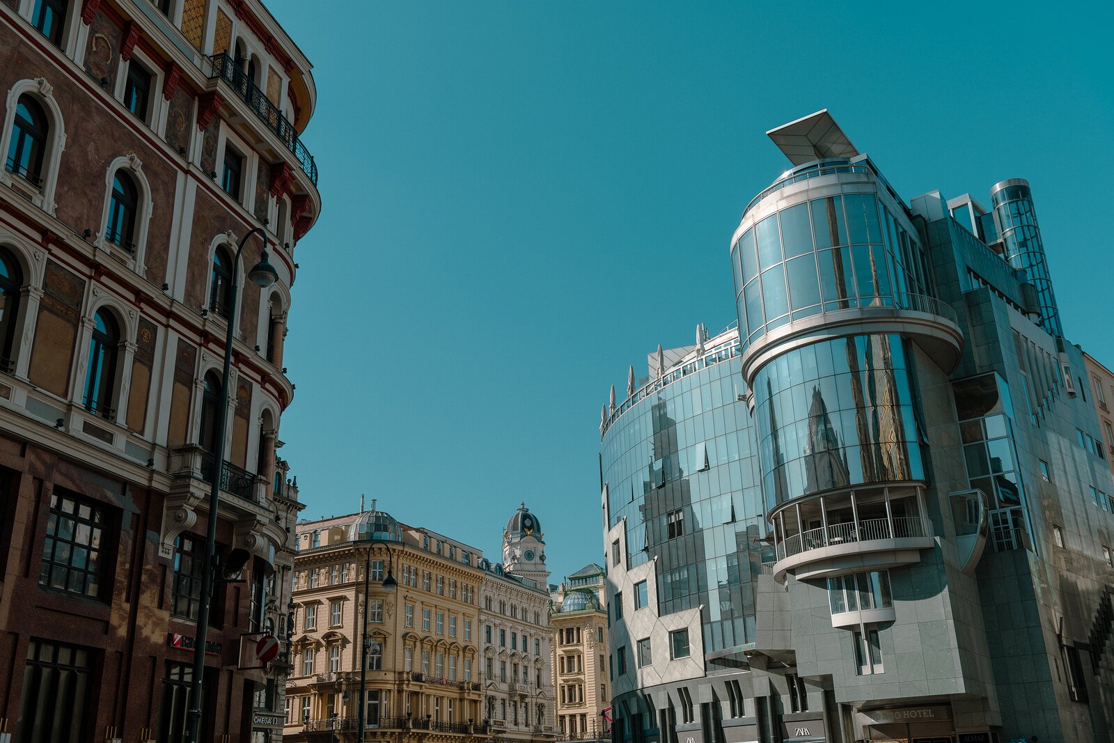 Mirror Contrast Glass-clad Haas Haus and neighbouring historic façades meet under a clear sky at a central Vienna intersection.