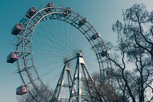 Nostalgic Carnival Upward view of the iconic Wiener Riesenrad Ferris wheel with red gondolas framed by bare tree branches.