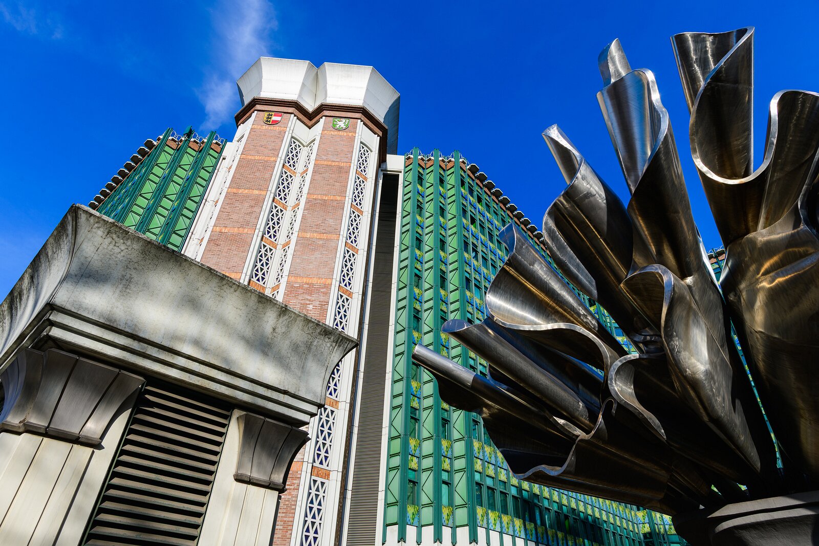 Futuristic Facade Oblique view of a modernist Vienna building with green panels and a stainless-steel flower-like sculpture against a clear blue sky.