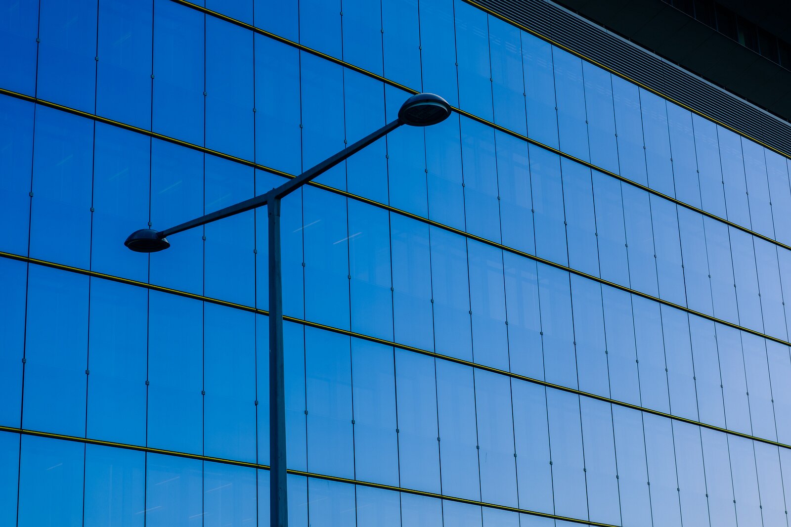 Urban Stillness Slim streetlamp silhouette set before a seamless blue glass curtain wall of a contemporary Vienna office block.