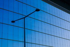 Urban Stillness Slim streetlamp silhouette set before a seamless blue glass curtain wall of a contemporary Vienna office block.