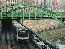 Historic Span Vienna U4 metro train emerging from a tunnel beneath an ornate green iron bridge along the Wien River.