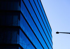 Blue Minimalism Sharp corner of a blue glass office tower with a lone streetlamp silhouette against a pale Vienna sky.