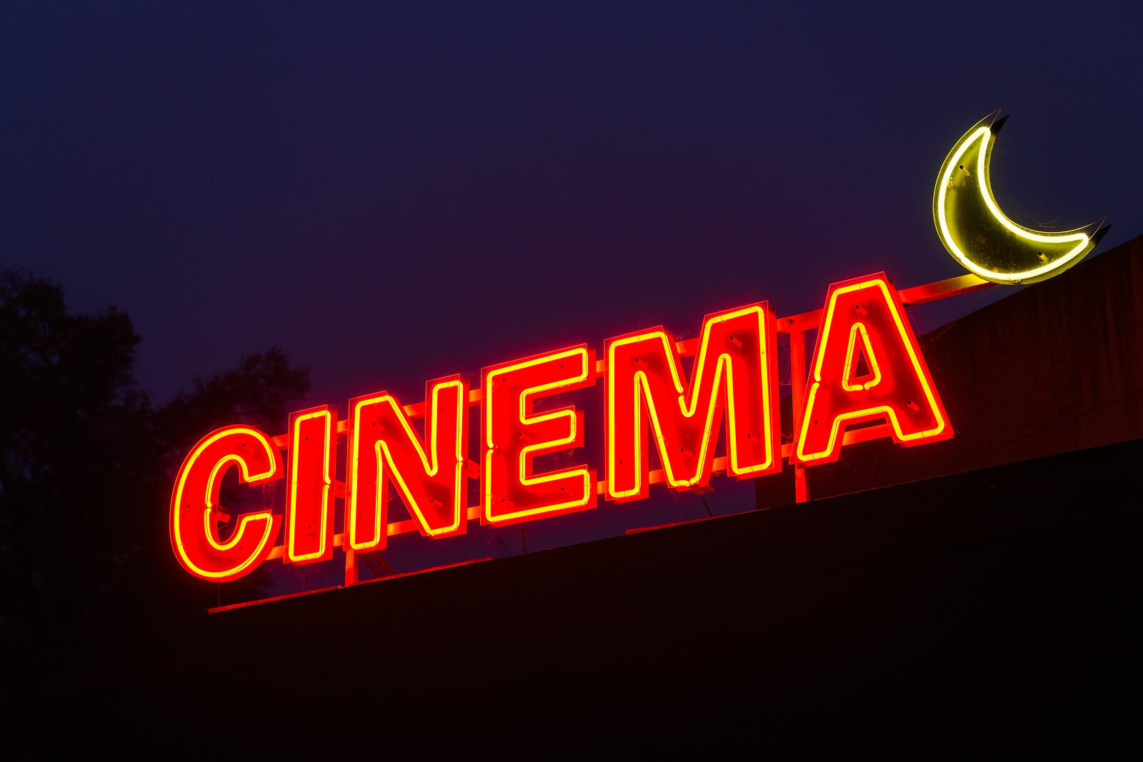 Movie Nights A red neon “CINEMA” sign glows beside a crescent moon against a darkening sky.