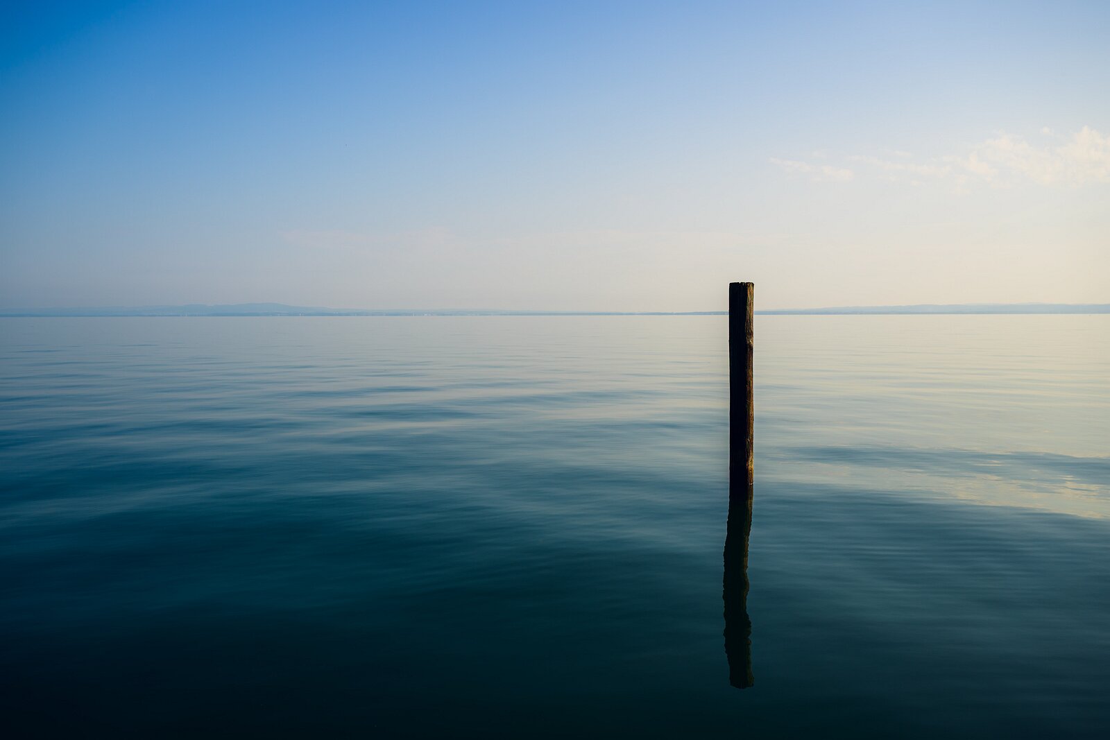 Solitary Reflection A solitary post stands in glassy, calm water under a soft-toned sky.
