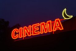 Movie Nights A red neon “CINEMA” sign glows beside a crescent moon against a darkening sky.